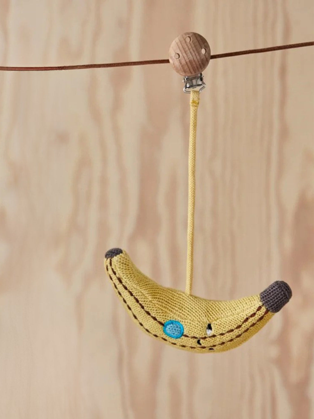 Knitted banana-shaped toy with a wooden bead on a string against a wooden background