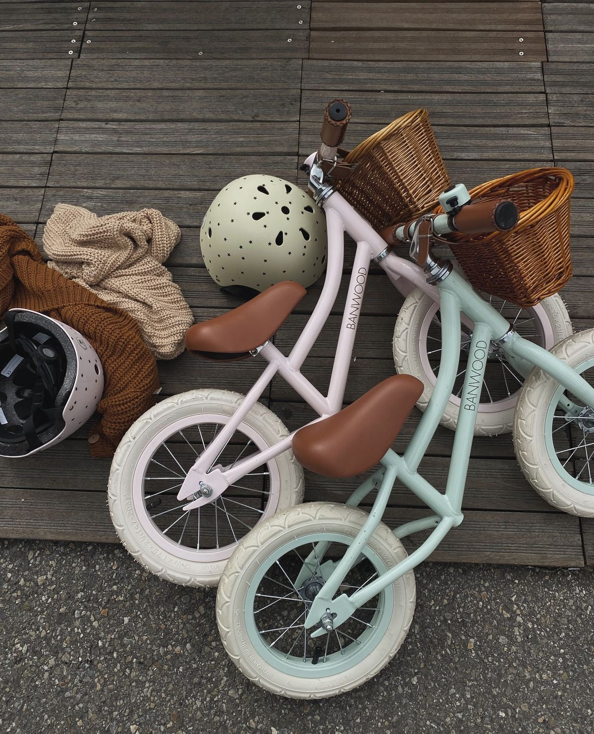 Two children's bicycles with baskets on a wooden deck.