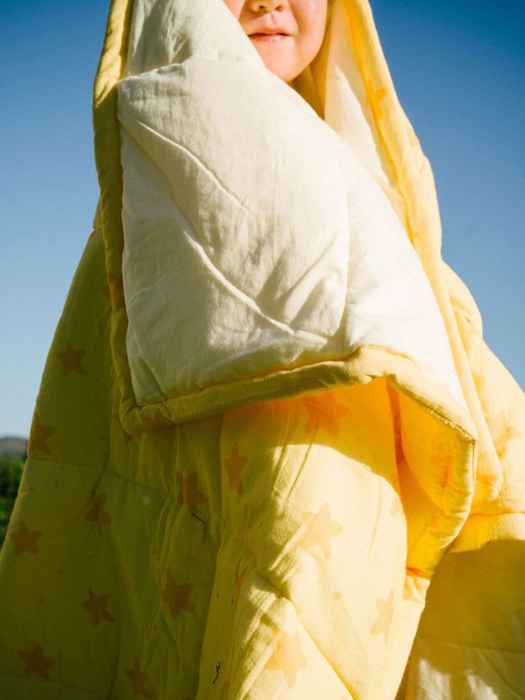 Kid wrapped in a blanket with star patterns against a clear blue sky