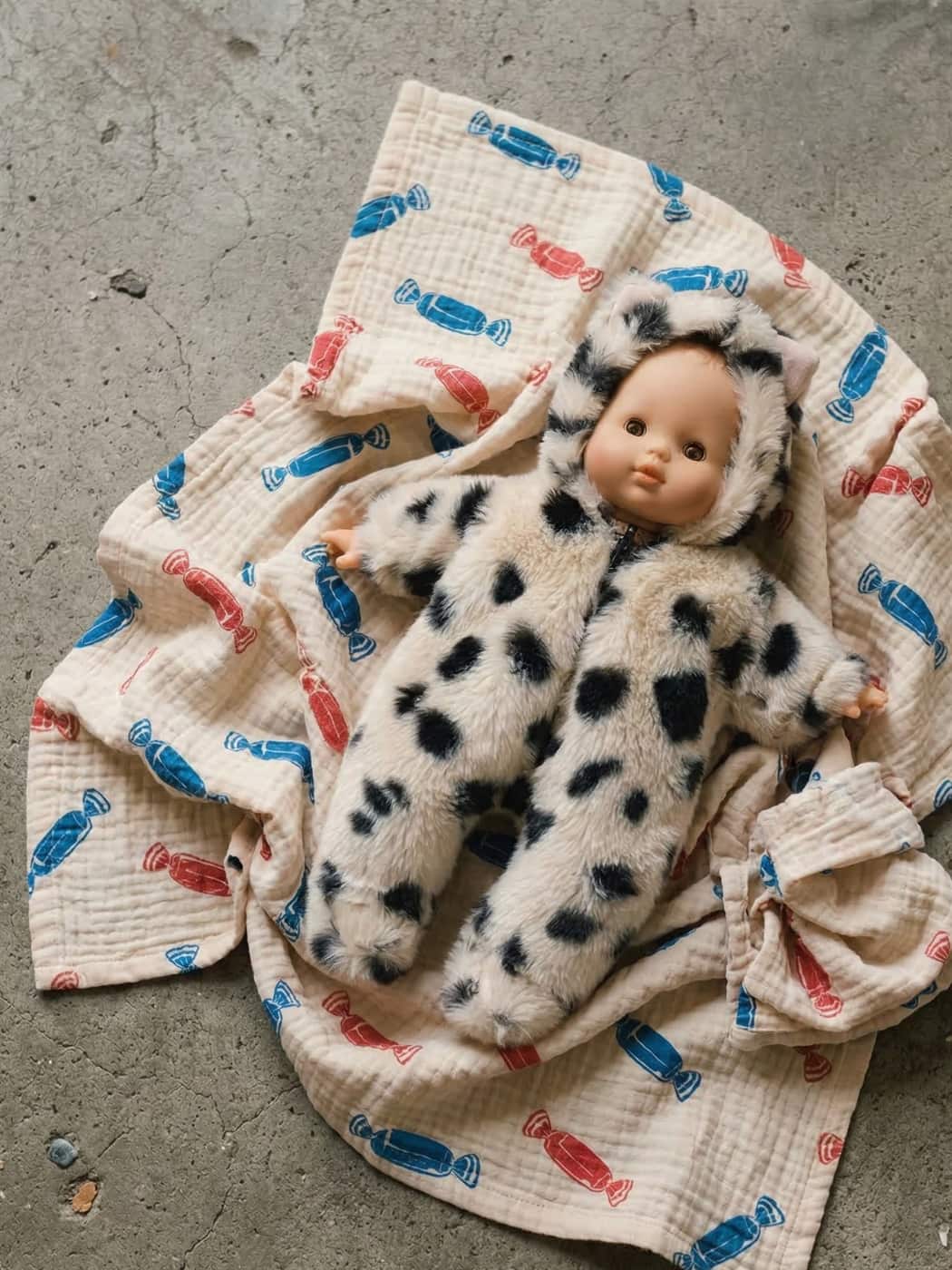 Baby doll in a spotted outfit on a textured blanket with colorful patterns.