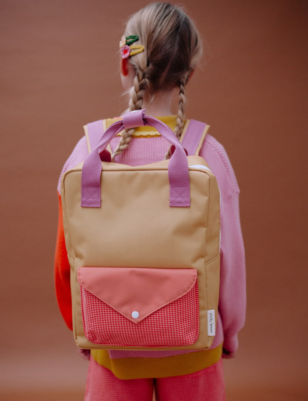 Child wearing a colourful sticky lemon backpack with a pink and yellow design against a brown background