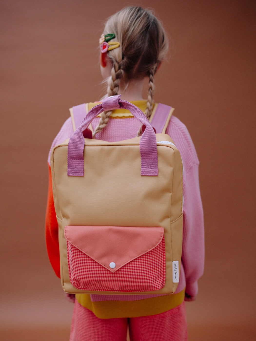 Child wearing a colourful sticky lemon backpack with a pink and yellow design against a brown background