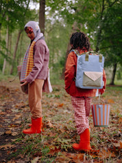 Two people walking in a forest with one carrying a blue backpack and the other holding a striped bag.